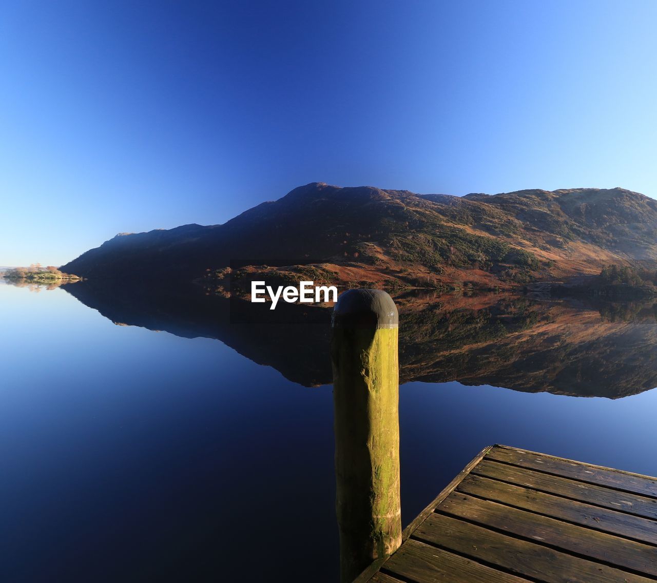 Scenic view of lake by mountains against clear blue sky