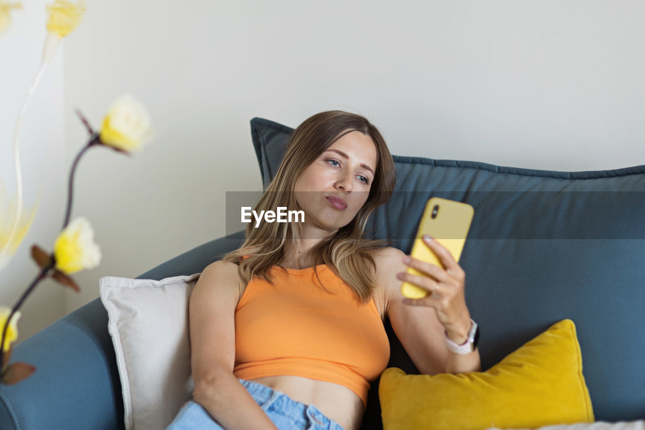 Young woman using mobile phone while sitting on bed at home