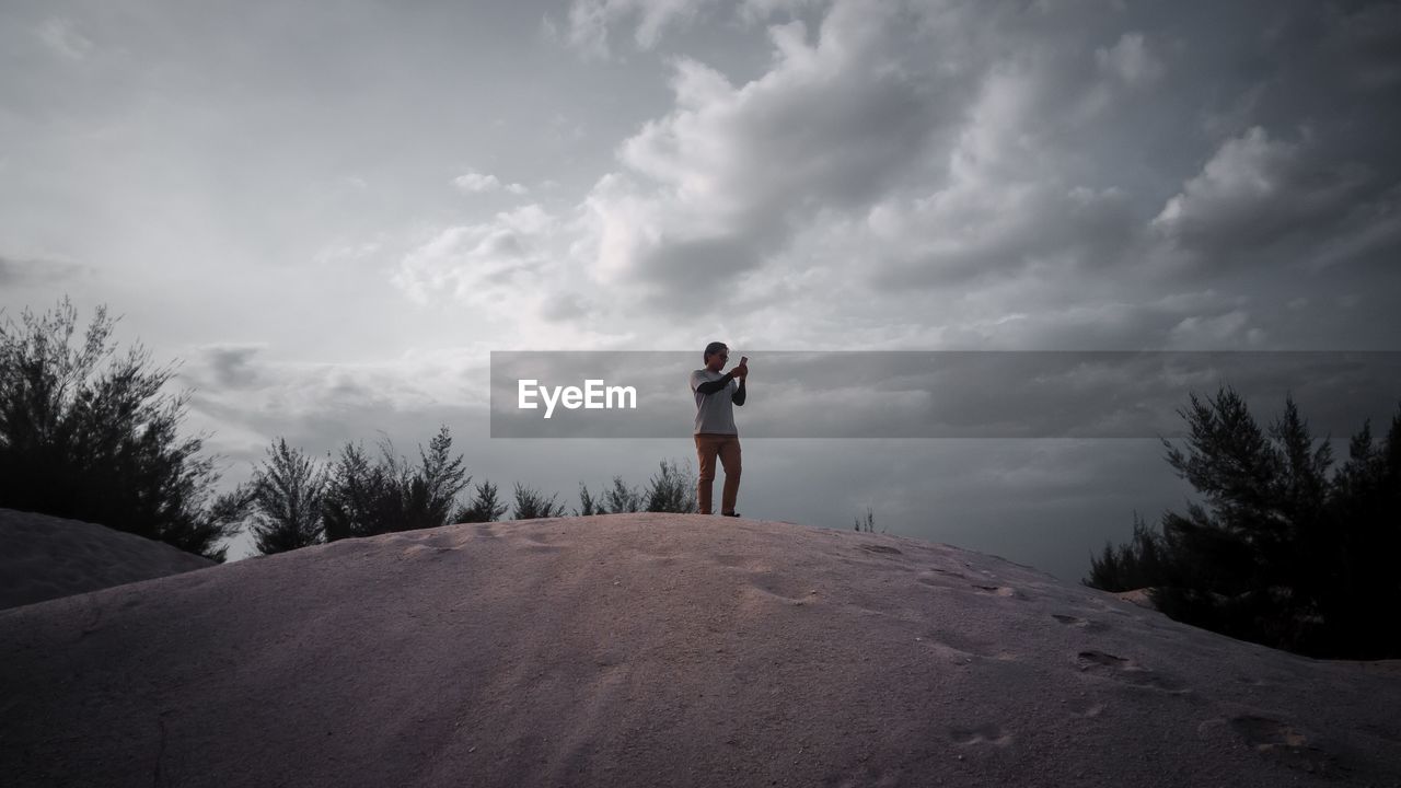 Man using mobile phone while standing on sand against sky