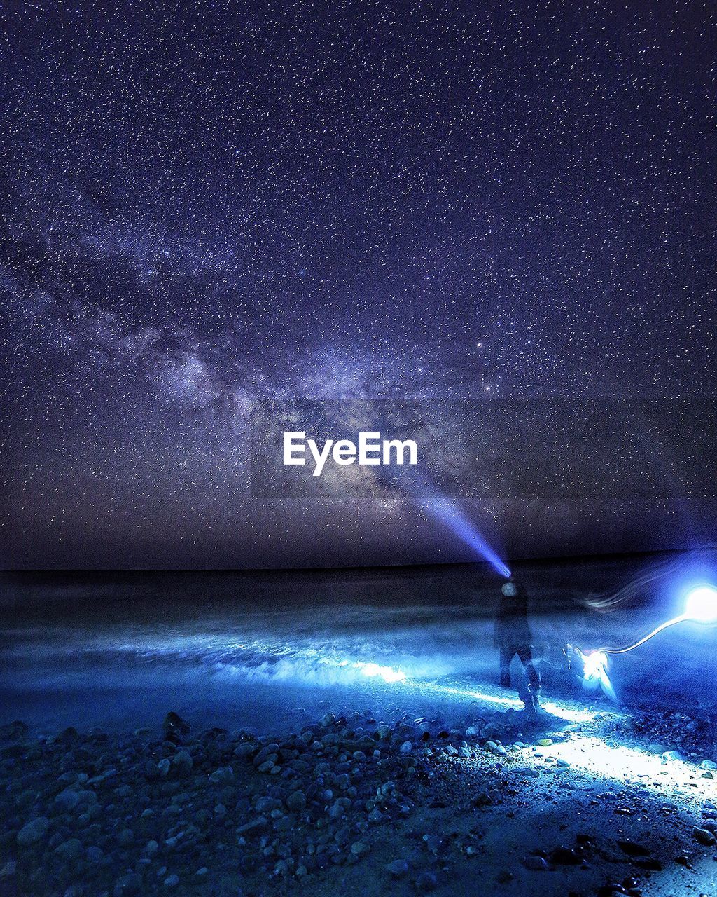 Rear view of person standing on shore holding flashlight against milky way