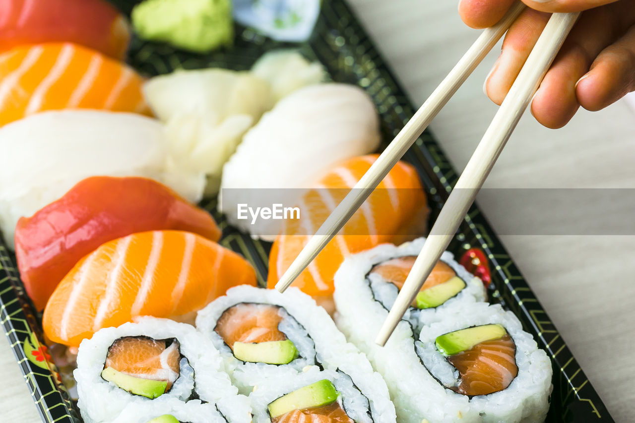 Cropped hand having sushi and sashimi in box on table