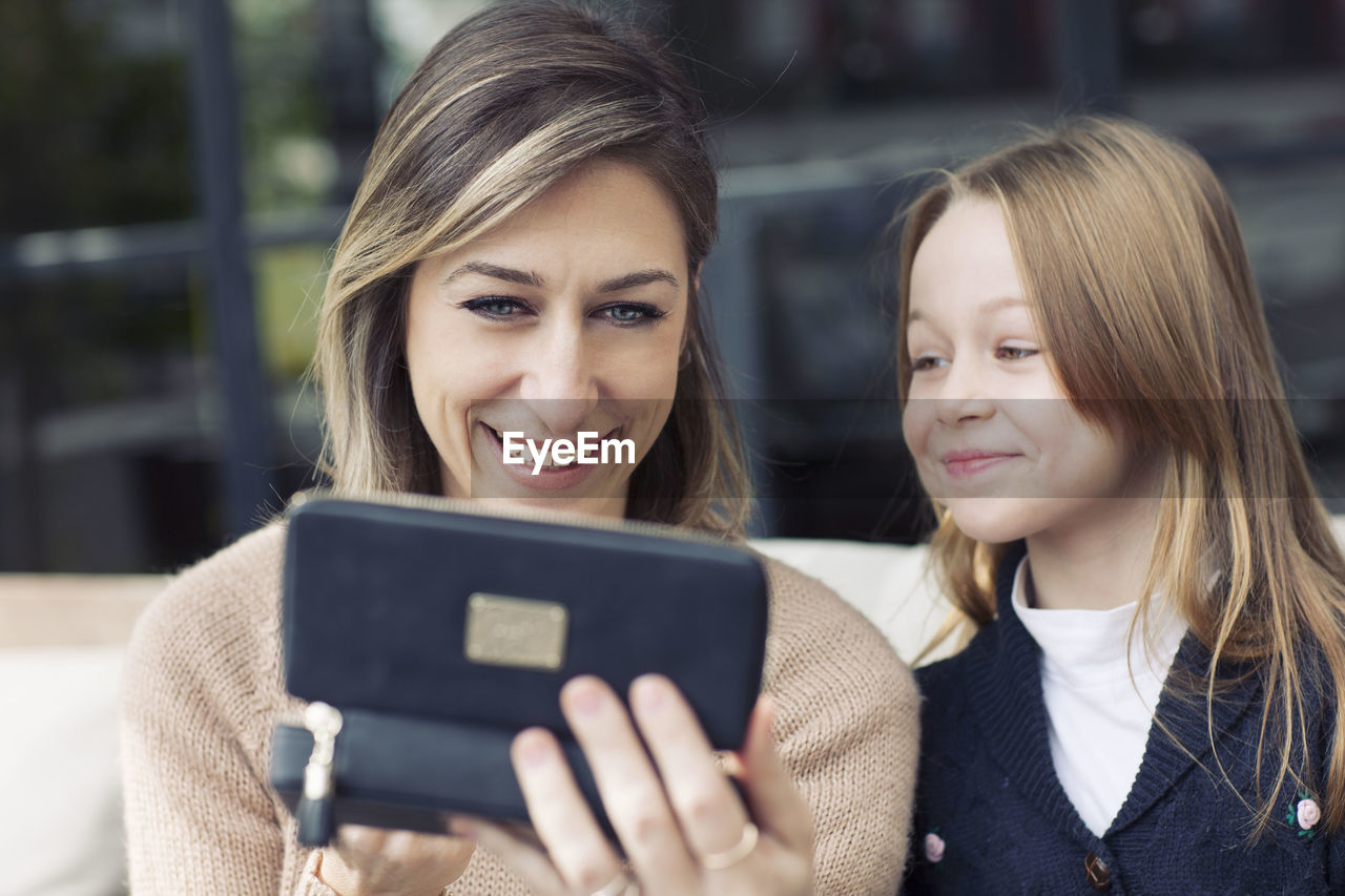 Close-up of mother and daughter using phone while sitting on sofa