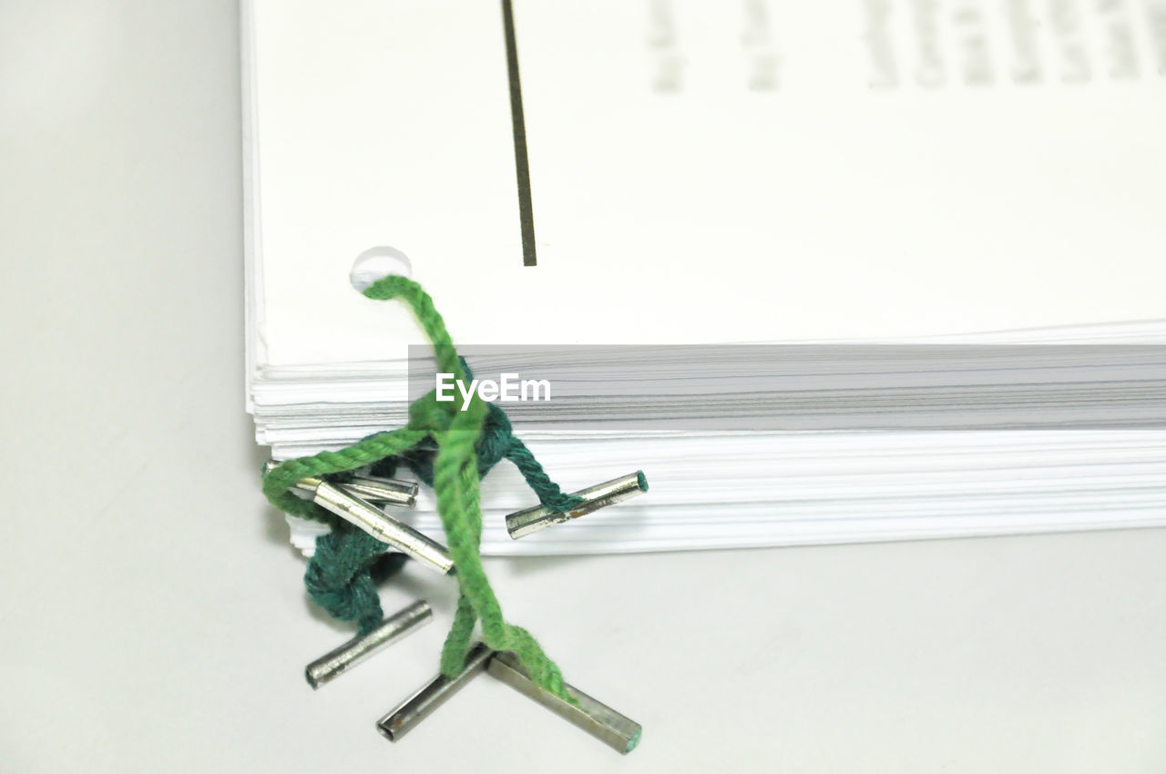 Close-up of green strings tied to papers over white background