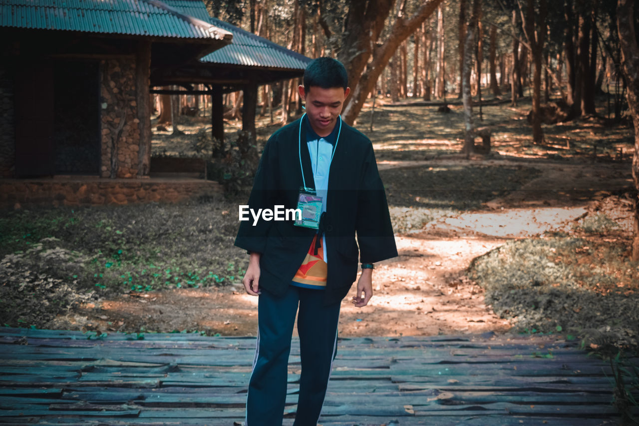 FULL LENGTH PORTRAIT OF YOUNG MAN STANDING AGAINST TREES