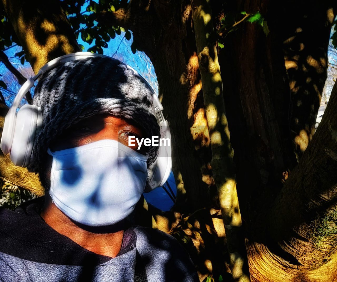 one person, portrait, tree, headshot, plant, front view, nature, clothing, leisure activity, day, sunlight, looking at camera, lifestyles, young adult, adult, blue, spring, outdoors, flower, costume, women, men, mask, forest, person, obscured face, casual clothing