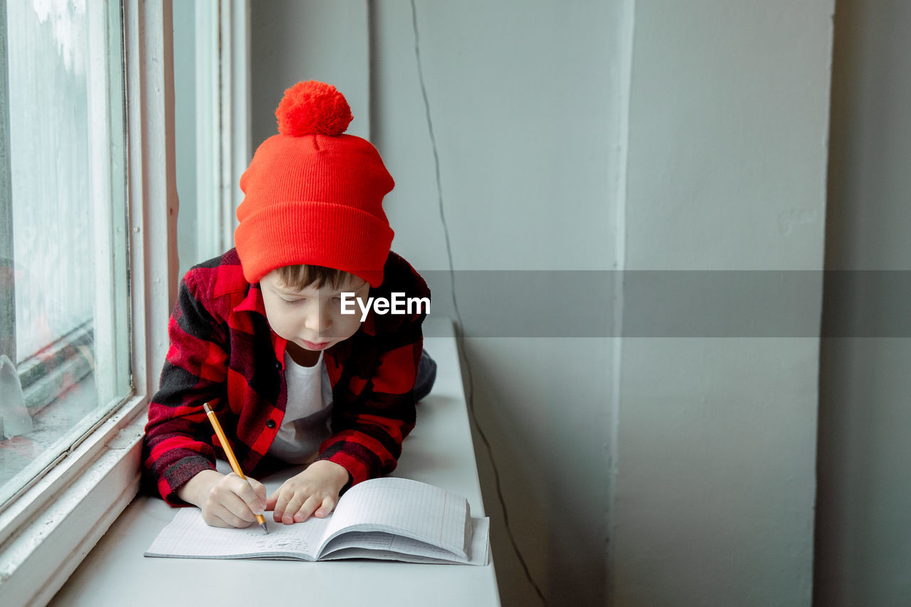 red, child, childhood, one person, men, sitting, hat, education, toddler, clothing, indoors, learning, looking, front view, portrait, publication, person, looking down, book, architecture, copy space, student
