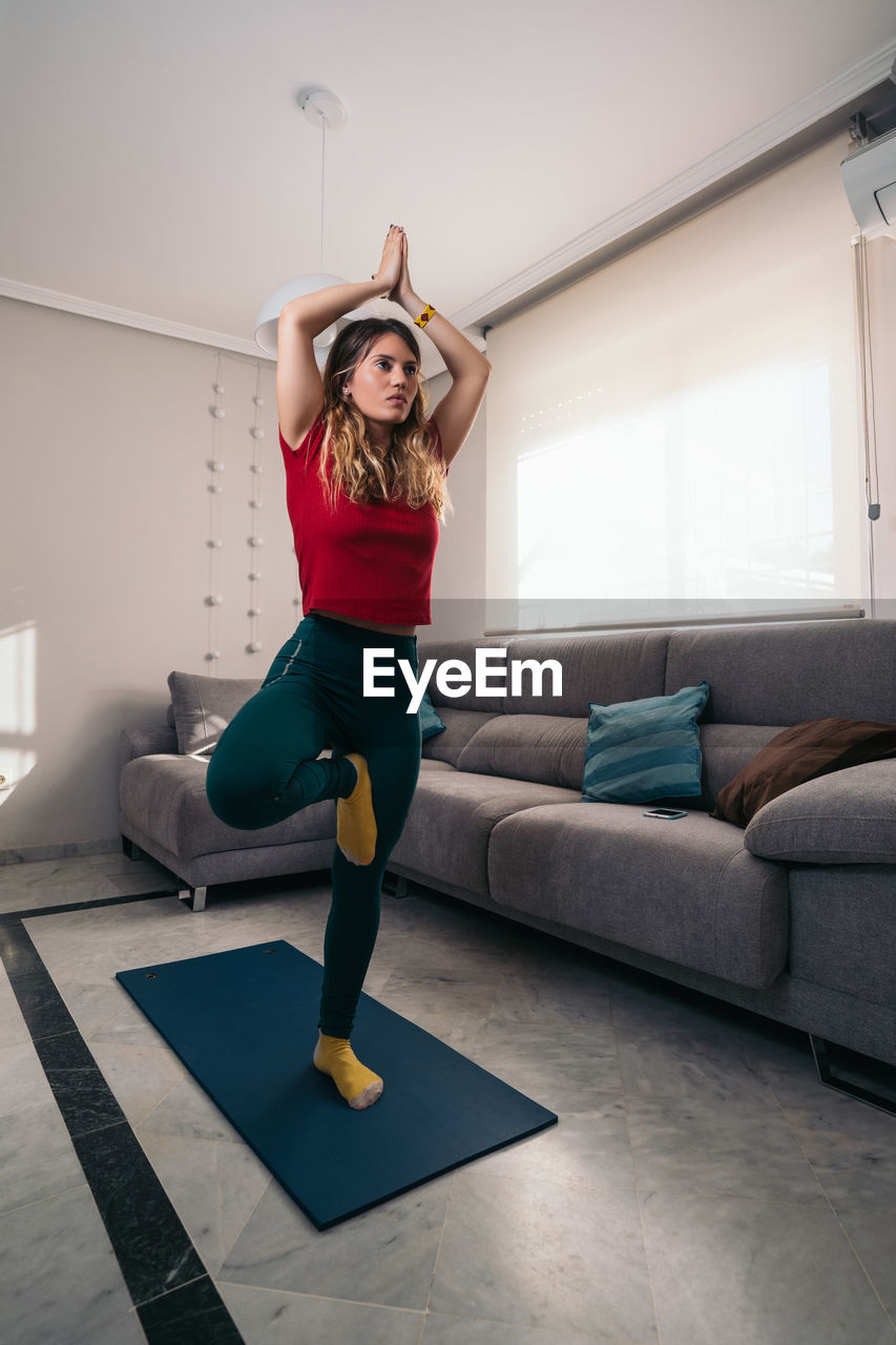 Full length of woman standing on sofa at home