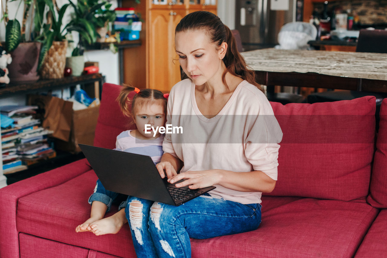 Caucasian mother with baby working on laptop from home. stay at home single at remote job online.