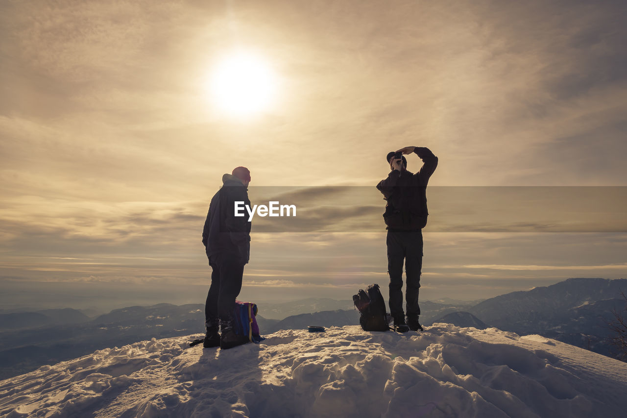 People standing on snow against sky during sunset