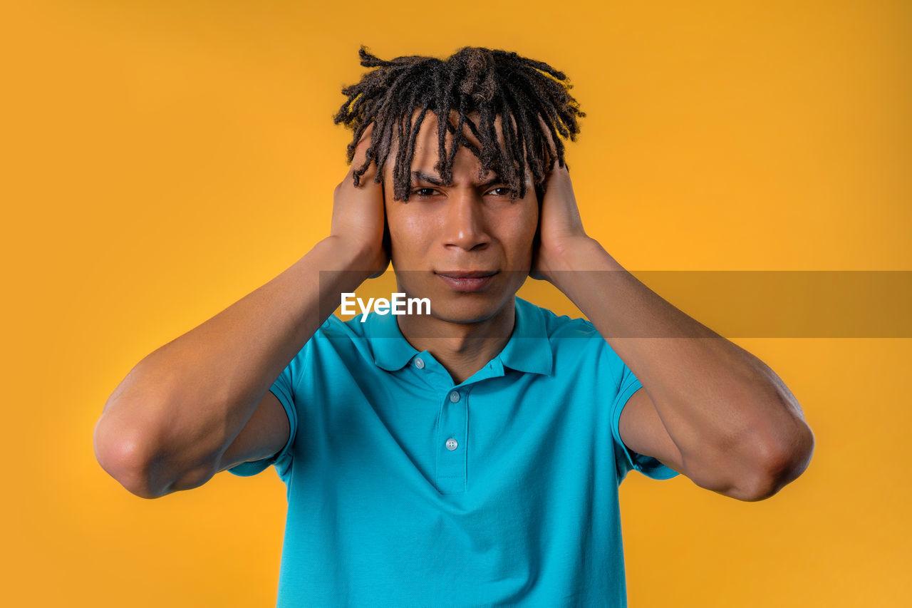 colored background, one person, studio shot, portrait, polo shirt, men, yellow background, yellow, emotion, indoors, front view, adult, waist up, negative emotion, clothing, frustration, hairstyle, child, young adult, person, facial expression, looking at camera, t-shirt, casual clothing, orange color, childhood, human face, hand, photo shoot, sadness, anger, teenager, standing