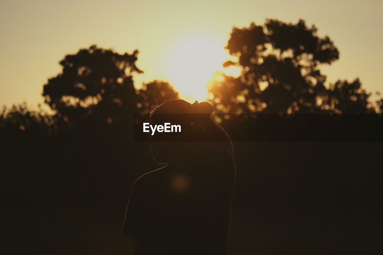 Silhouette woman standing by tree against sky during sunset