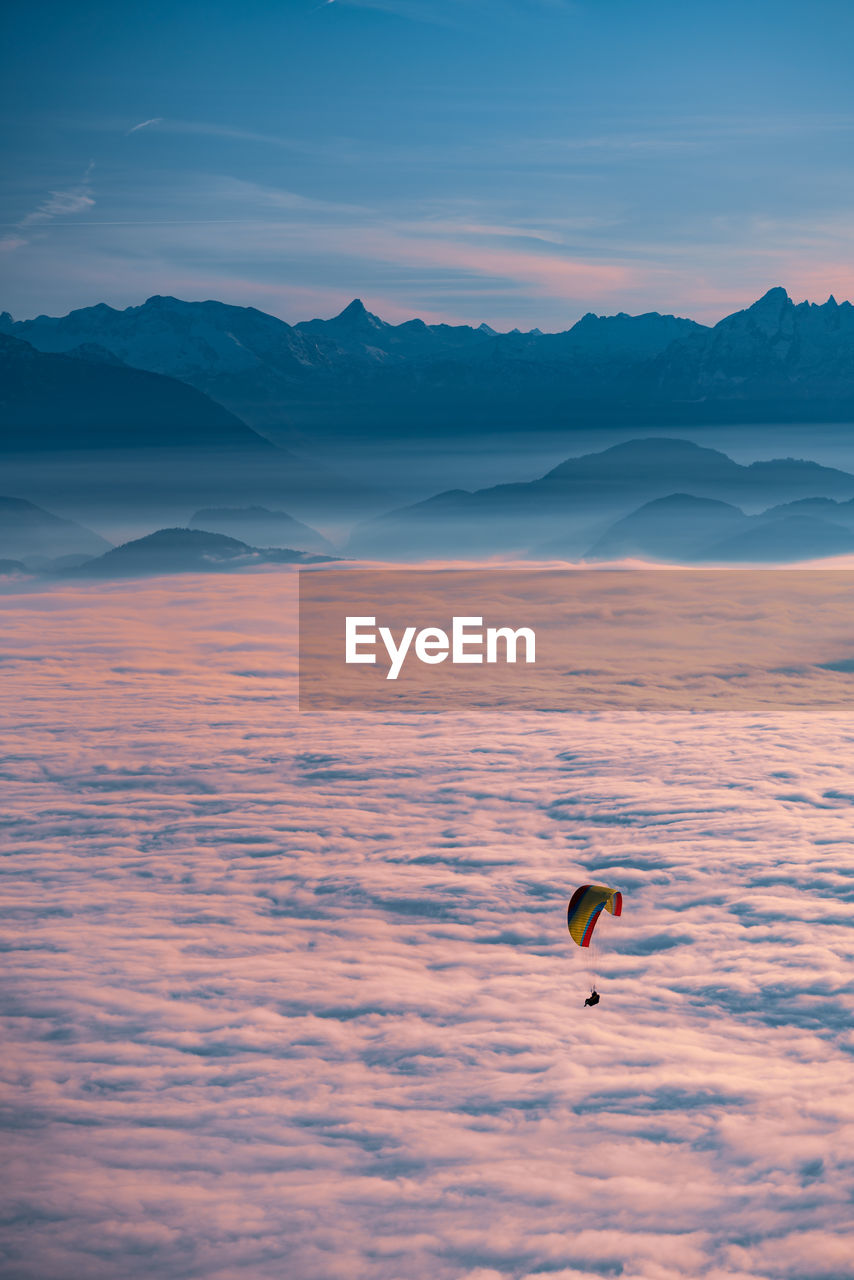 Silhouette of person paragliding over cloudscape