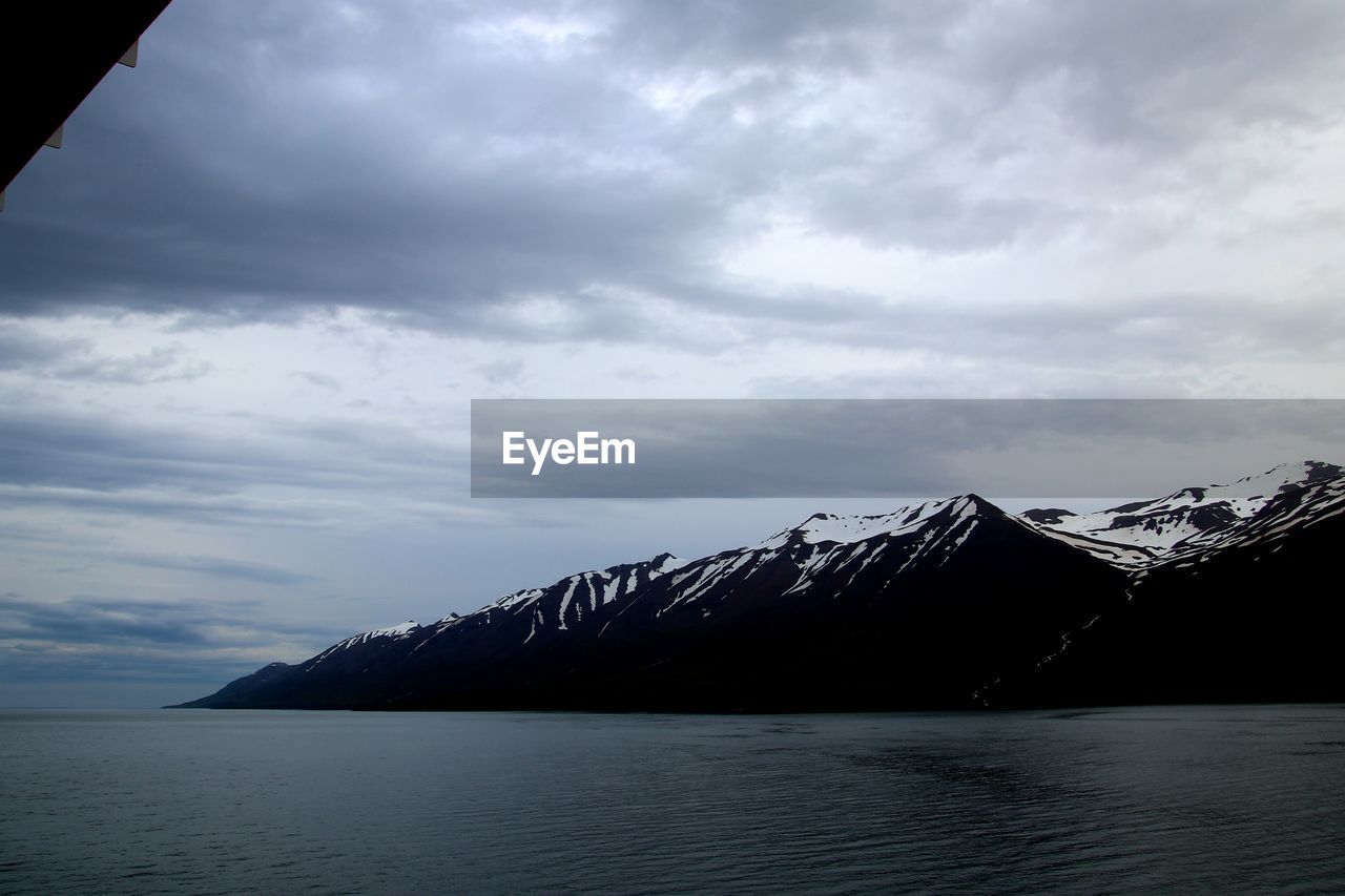 Scenic view of sea by snowcapped mountains against sky