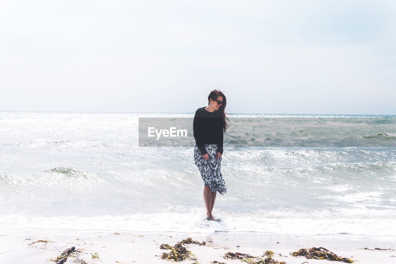 Full length of woman standing on beach against clear sky