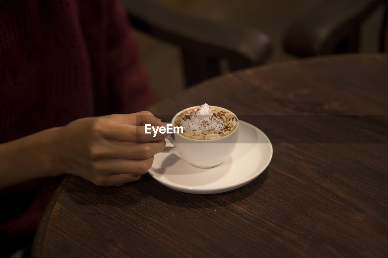 Close-up of woman hand holding coffee cup on table