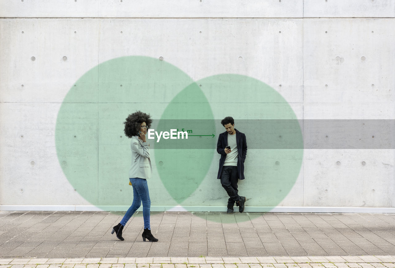 Two overlapping circles visualizing social distancing covering man and woman using smart phones outdoors