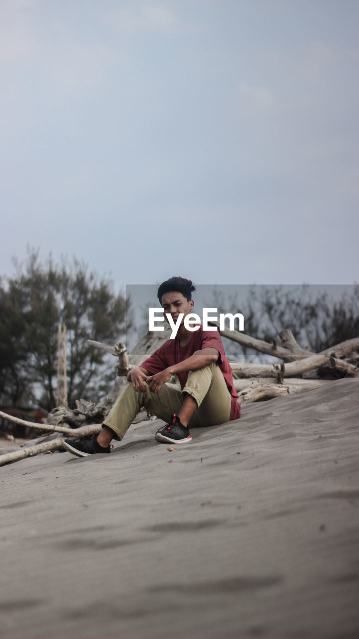 Portrait of man sitting on sand against sky