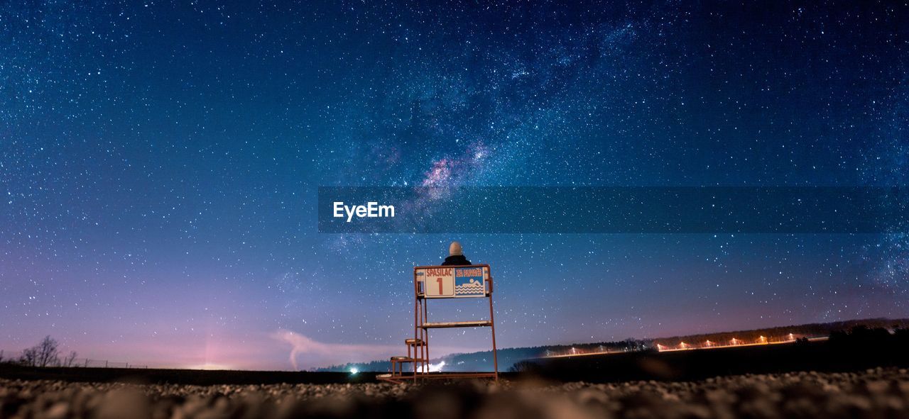 Rear view of person sitting on lifeguard hut at beach against star field