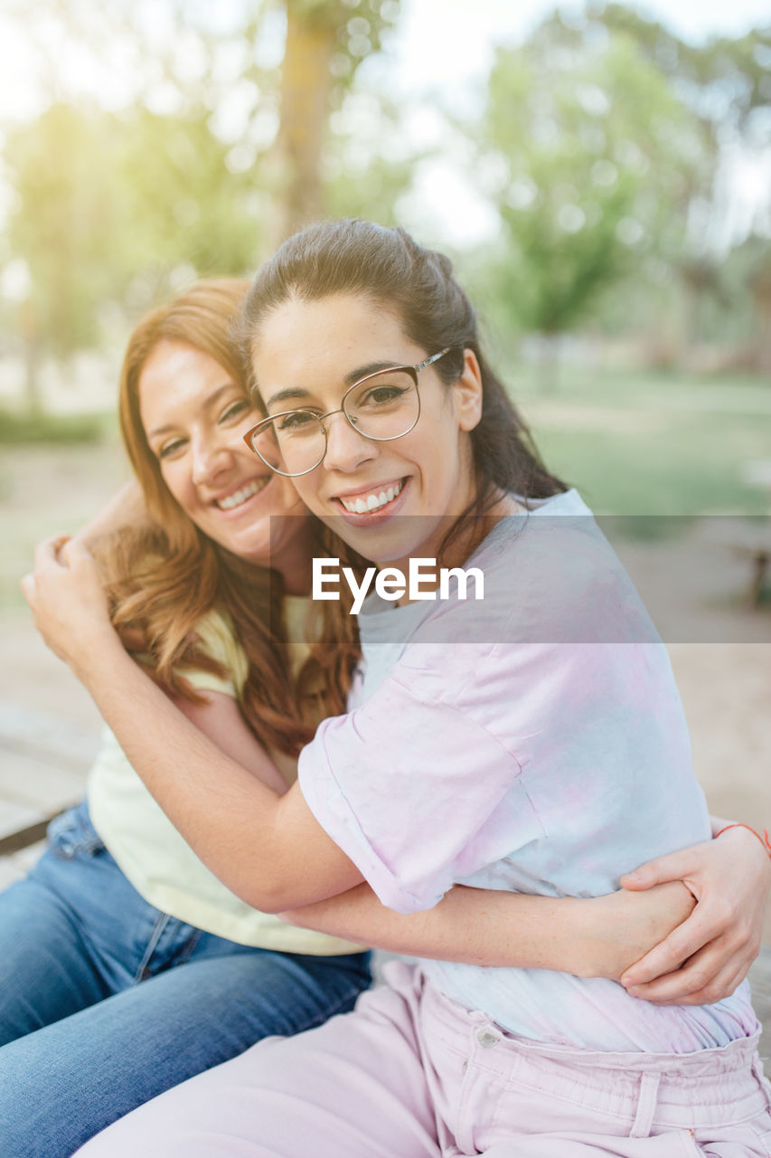 Two happy girlfriends embracing looking at camera smiling