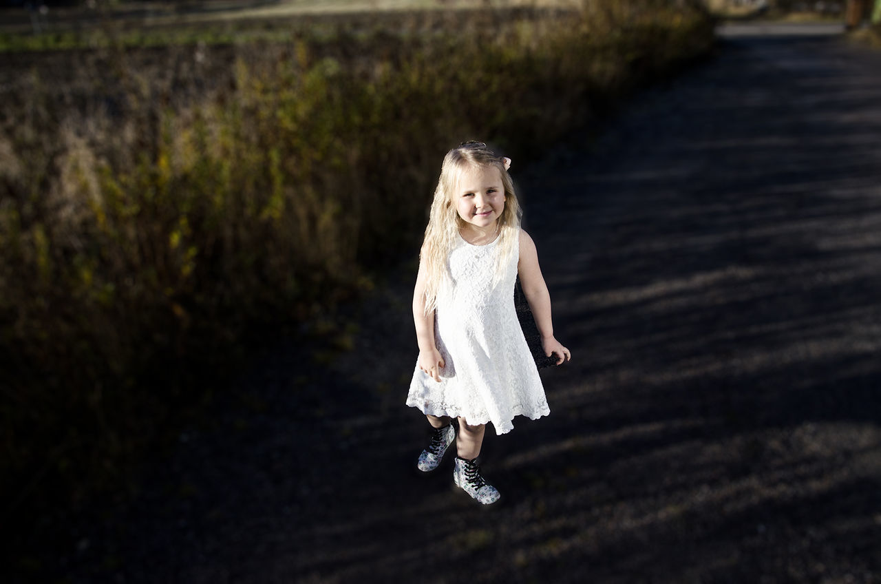 Portrait of cute girl wearing white dress walking on field