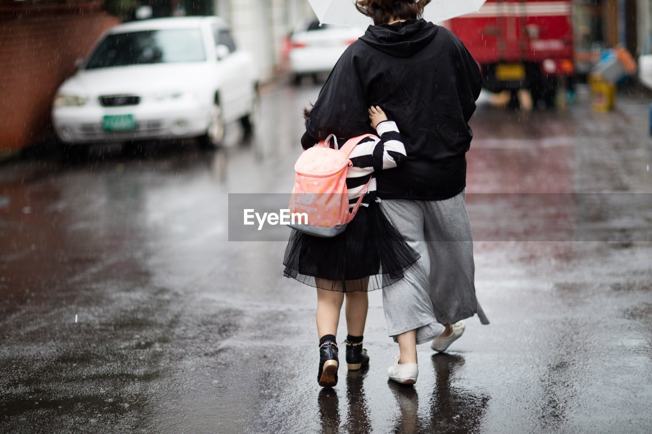 Rear view of mother and daughter walking on wet street