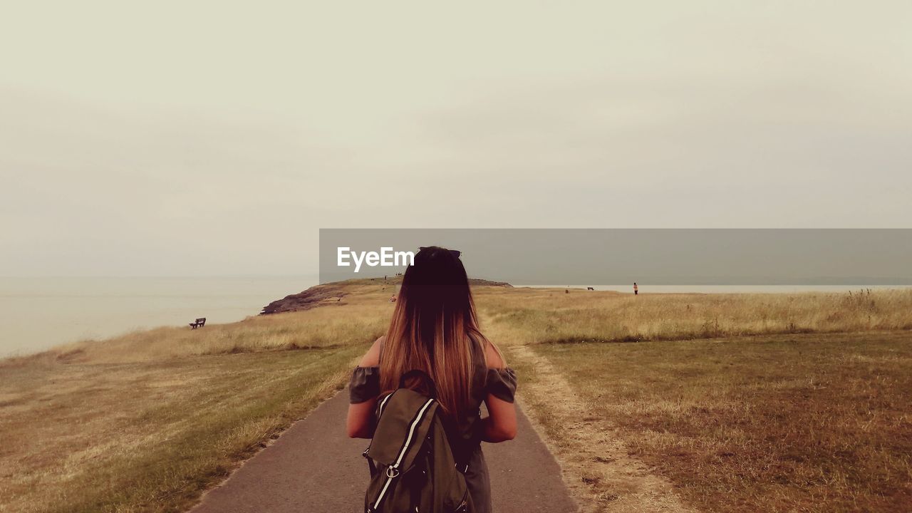 Rear view of woman with backpack standing on road against sky