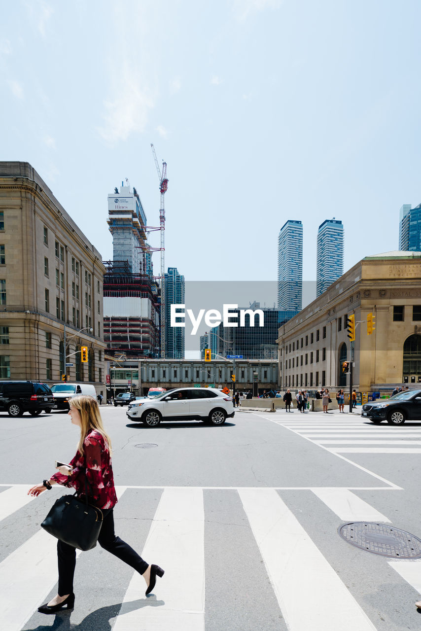 WOMAN ON STREET BY BUILDINGS AGAINST SKY