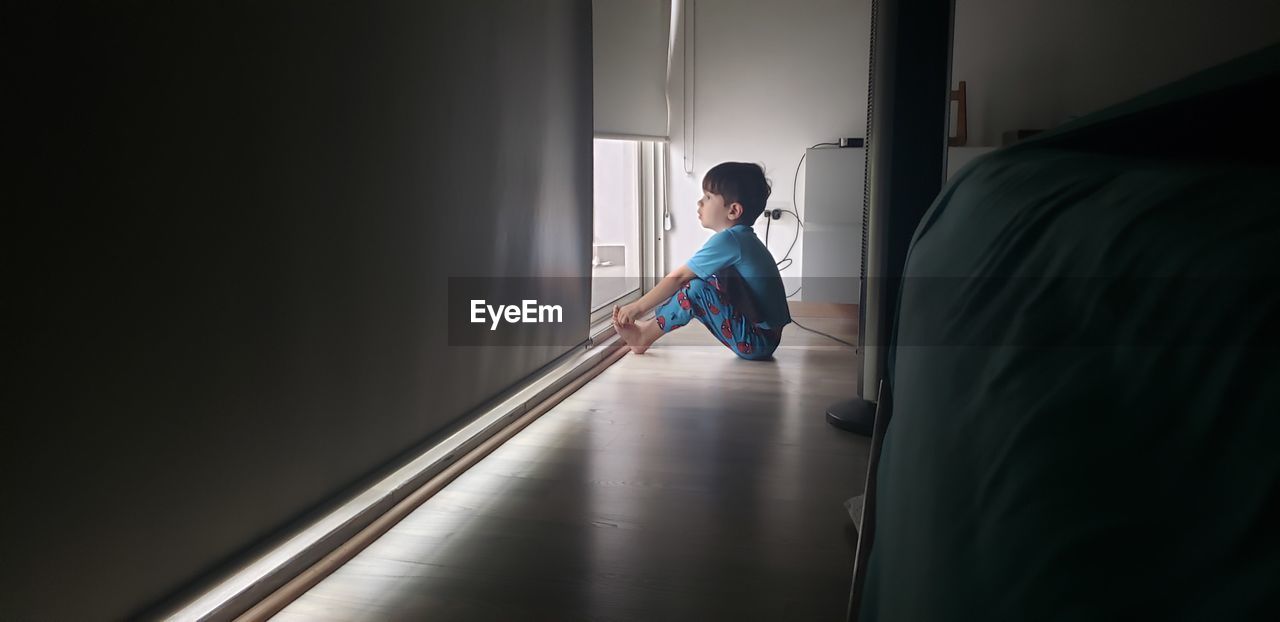 Side view of boy looking through window at home