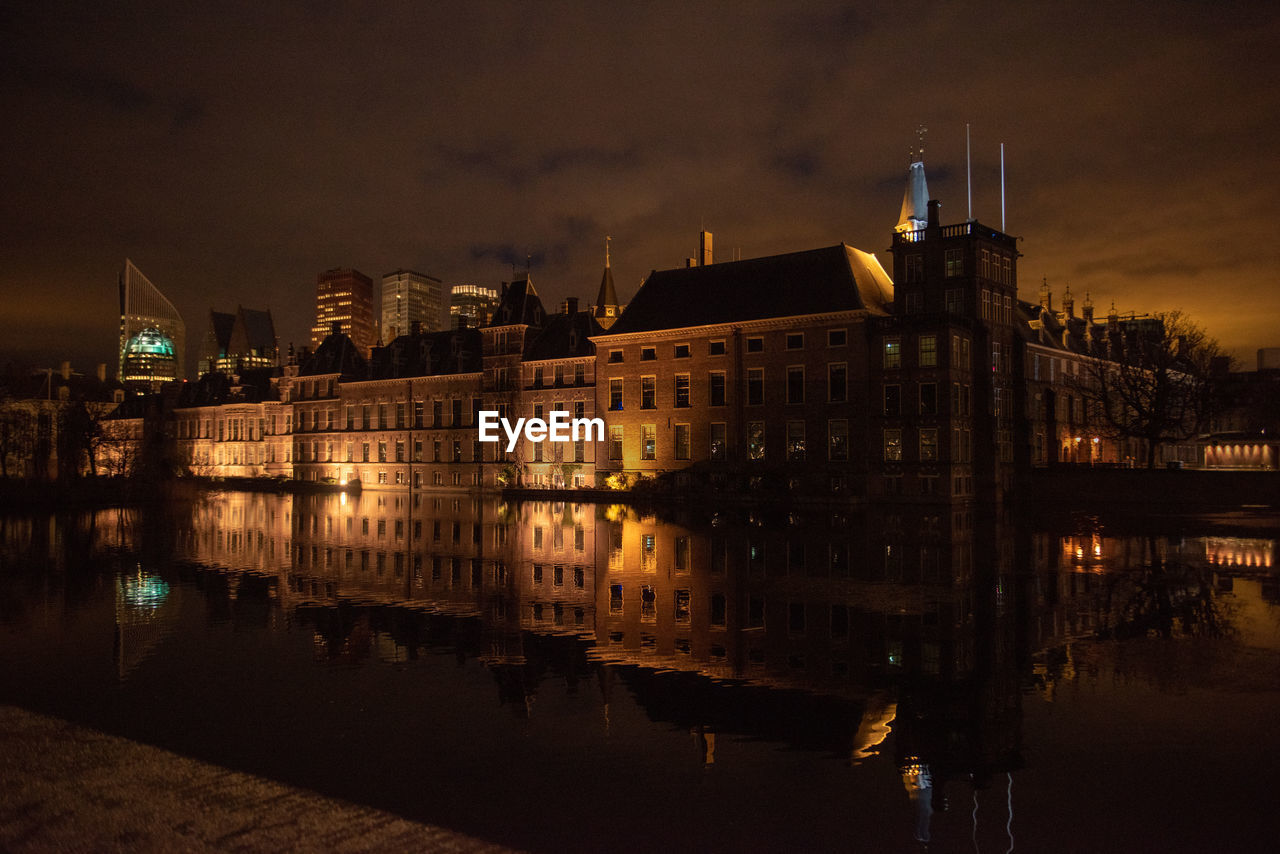 Illuminated buildings by river against sky at night