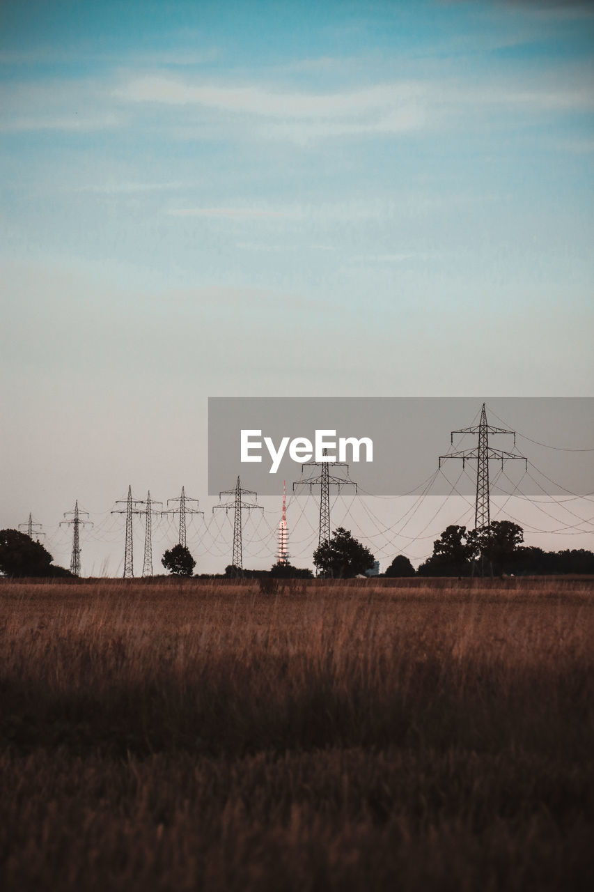 Electricity pylons on field against sky