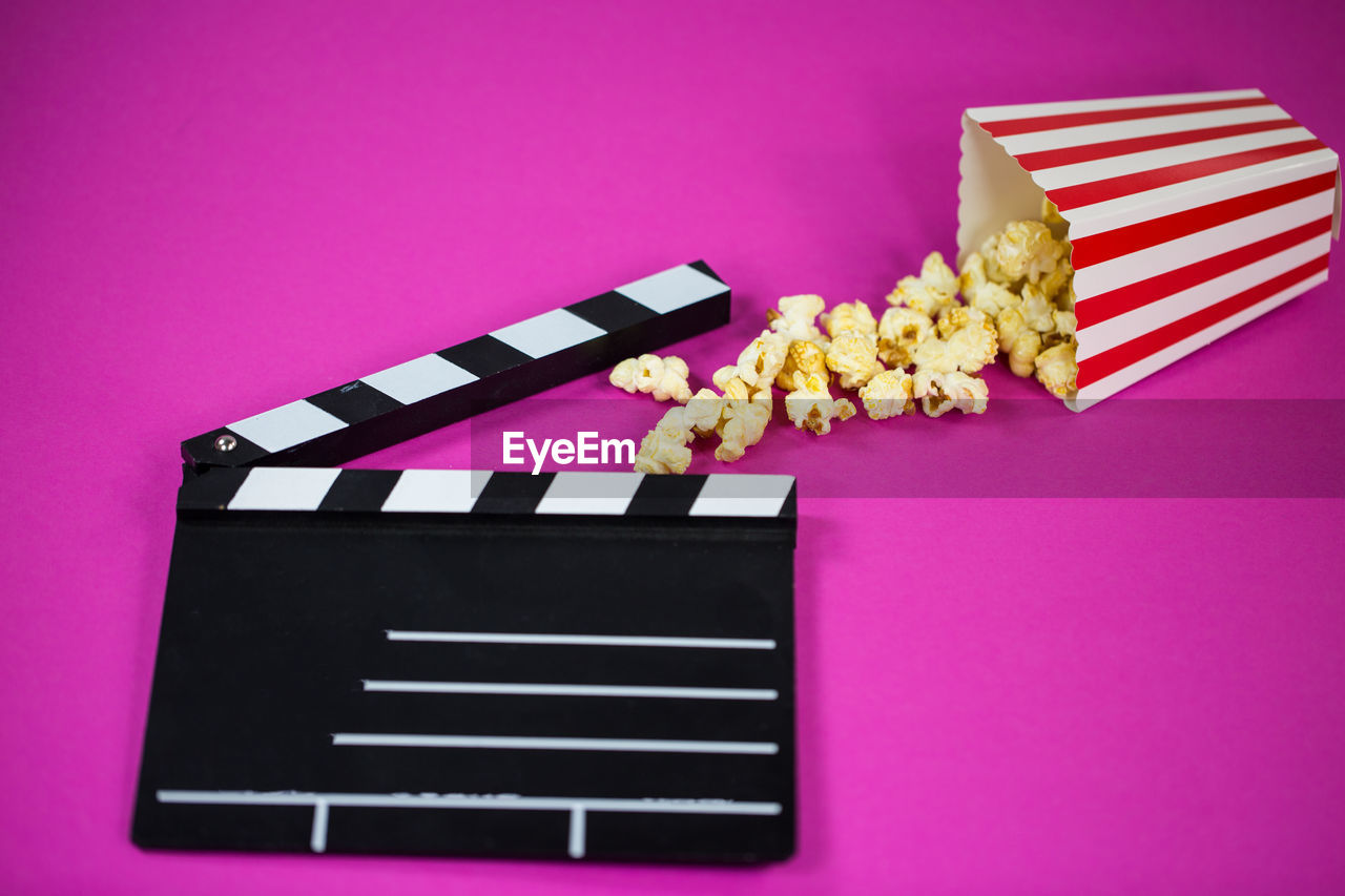 High angle view of popcorn and film slate over pink background