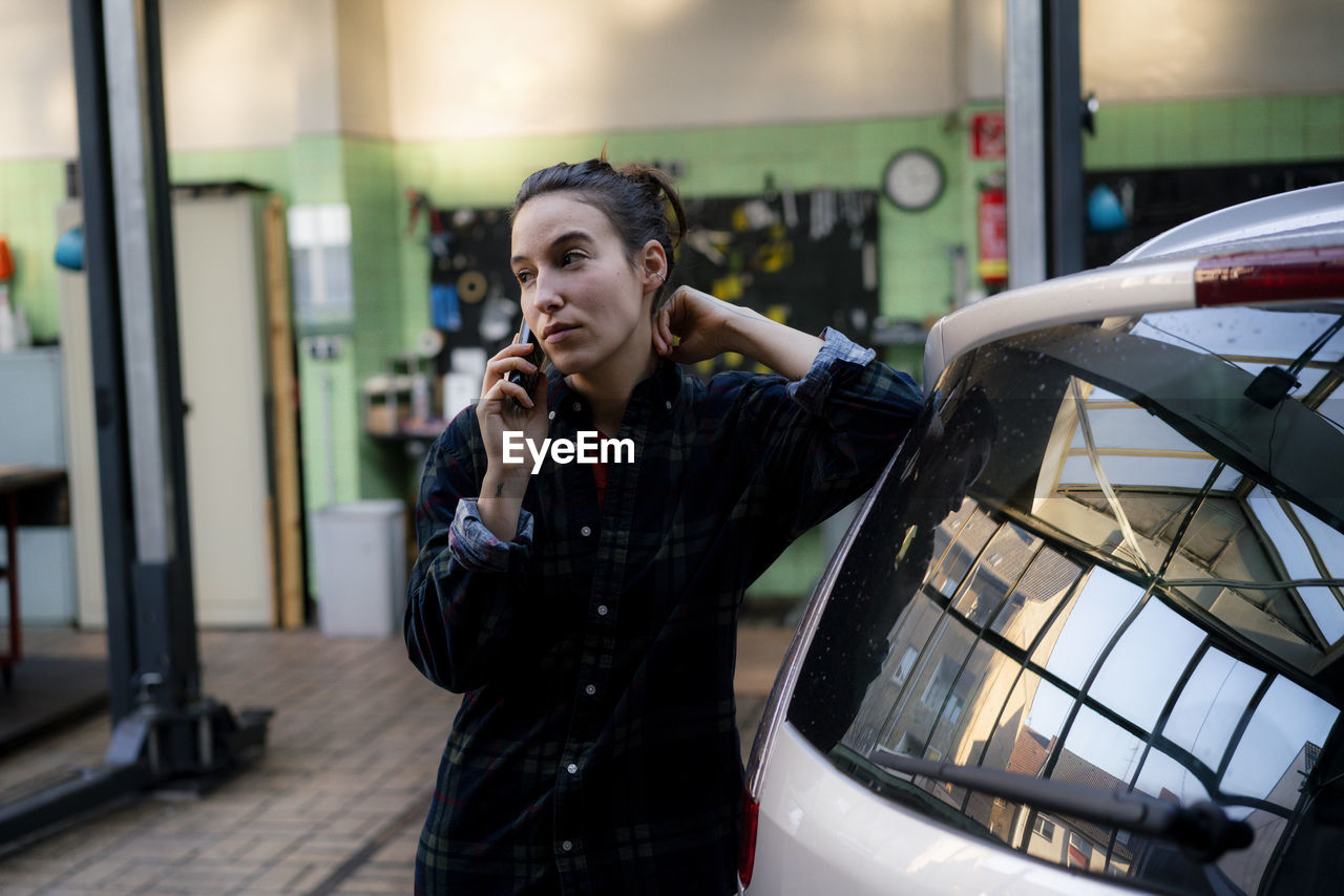 Female mechanic looking away talking on smart phone at repair shop