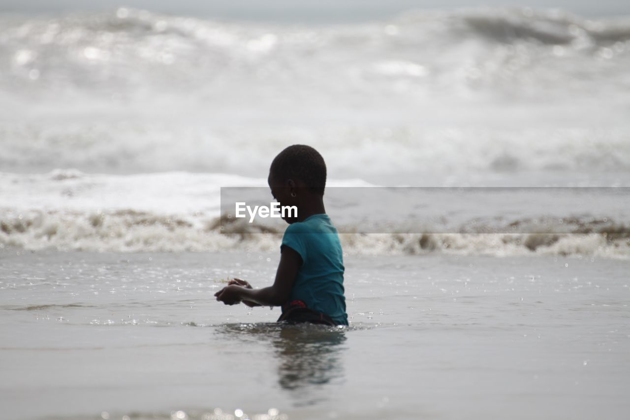 REAR VIEW OF BOY ON BEACH AGAINST SKY