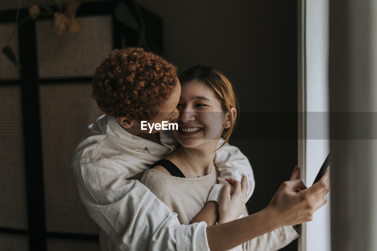 Happy non-binary couple embracing at home