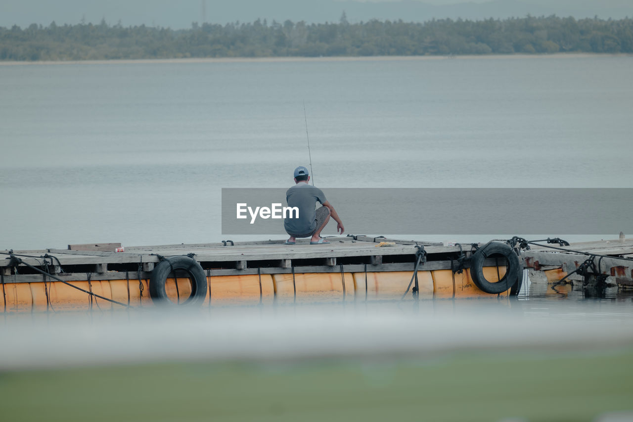 Rear view of man fishing while crouching on pier