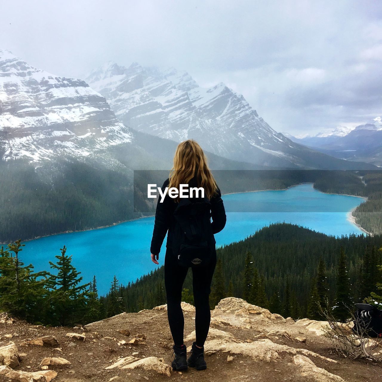 Rear view of woman standing on cliff against mountain against sky