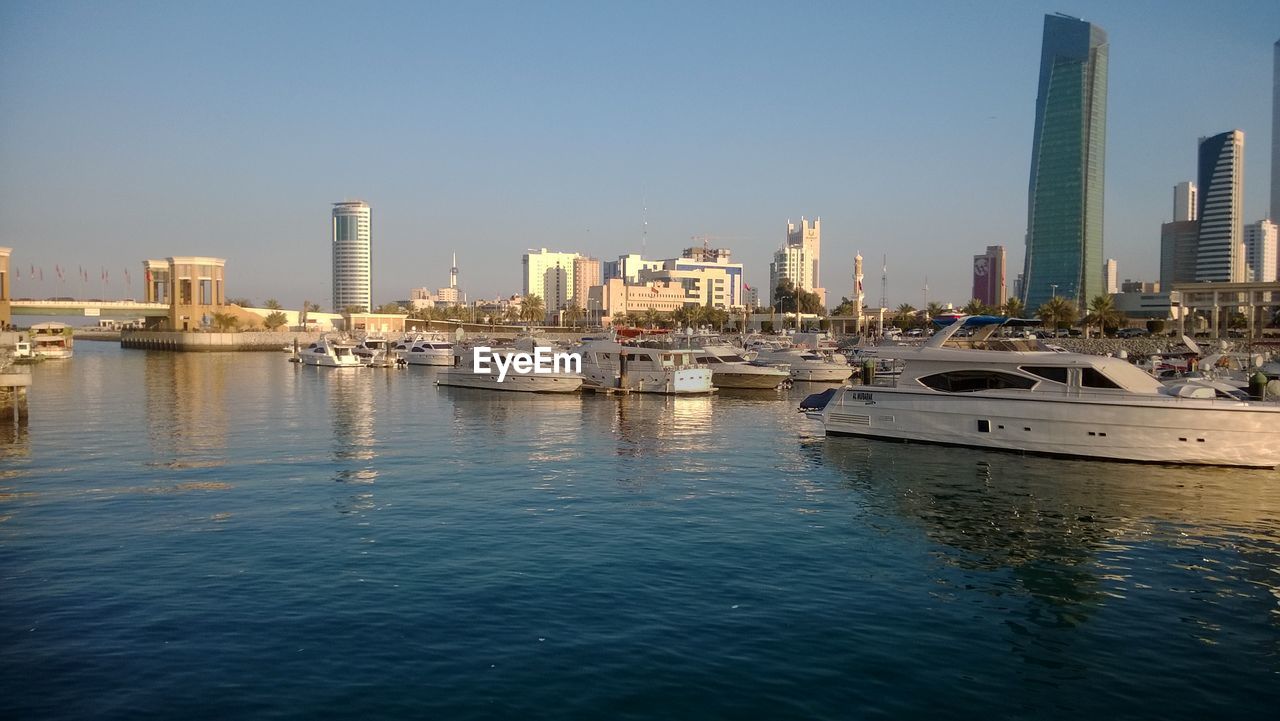 Boats moored in sea by city against clear sky