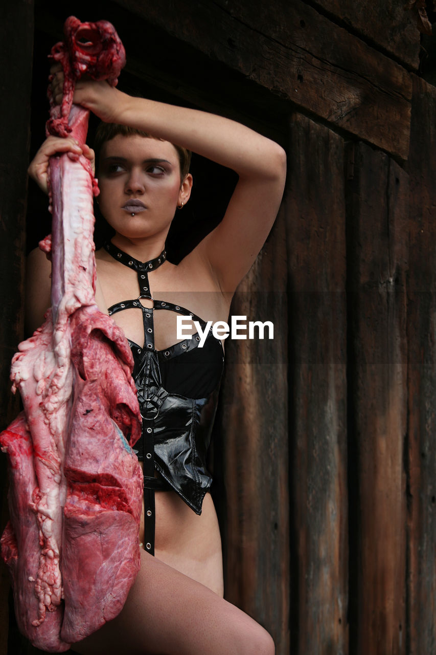 Seductive woman holding raw beef against wooden wall