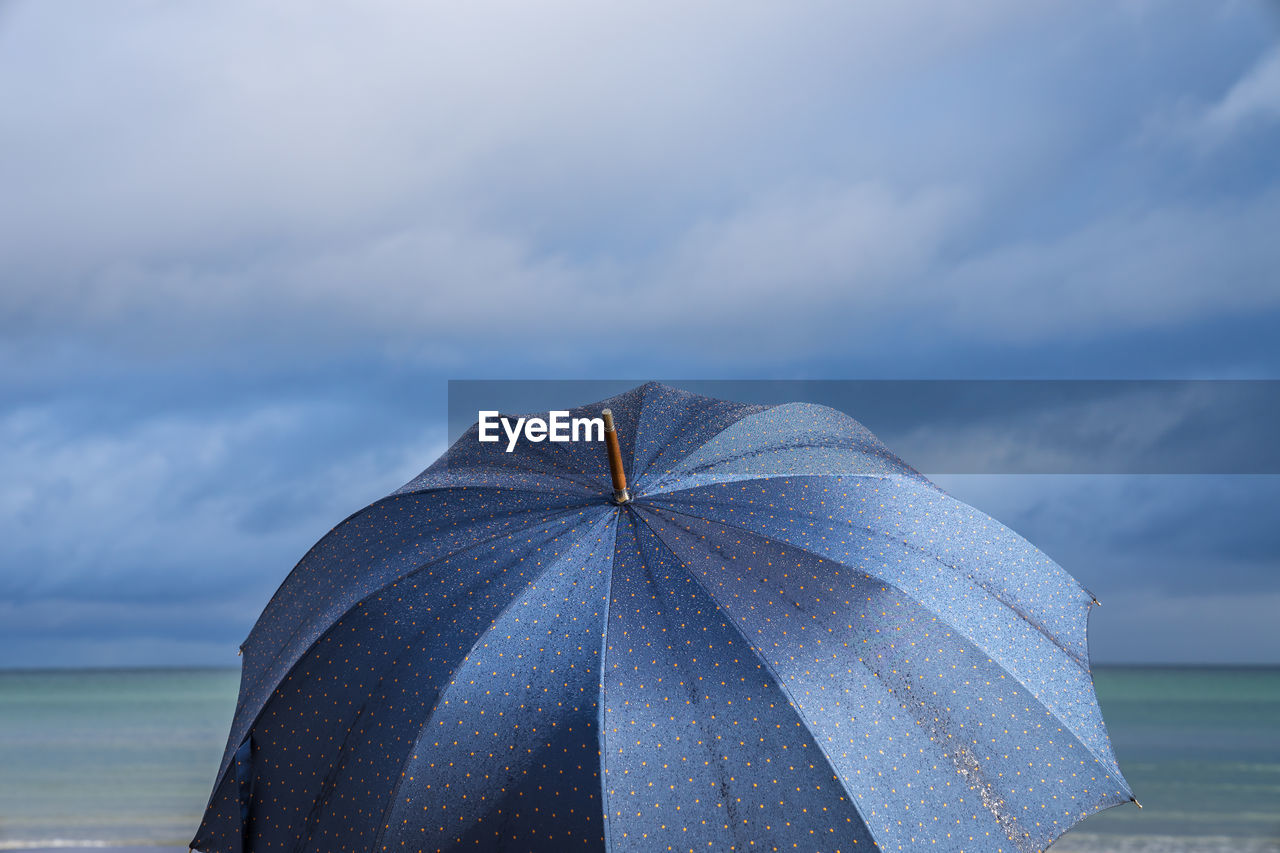 Close-up of open umbrella against cloudy sky at beach