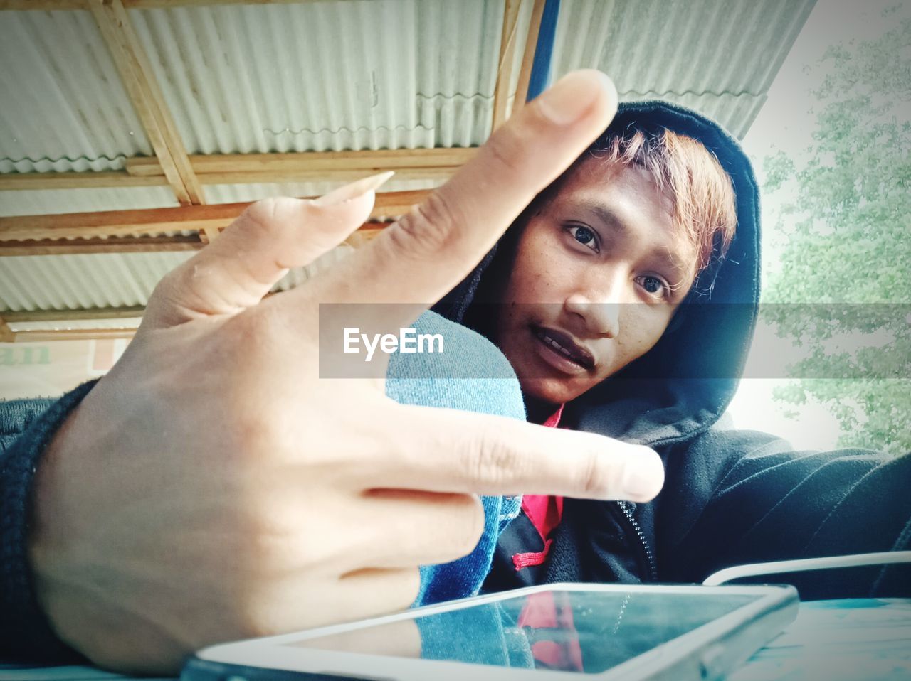 Portrait of young man gesturing peace sign against ceiling