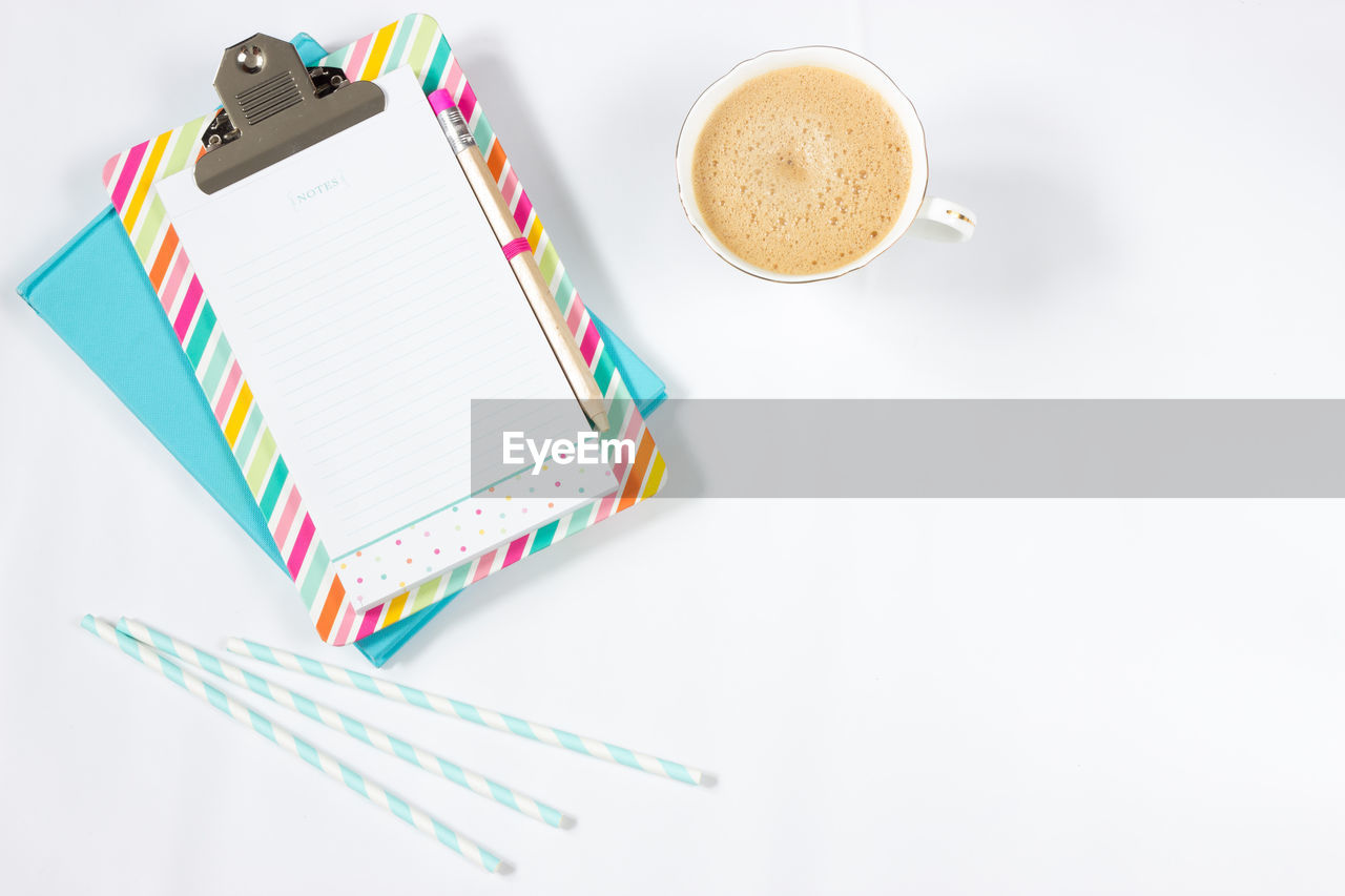 High angle view of coffee cup with drinking straws and note pads on table