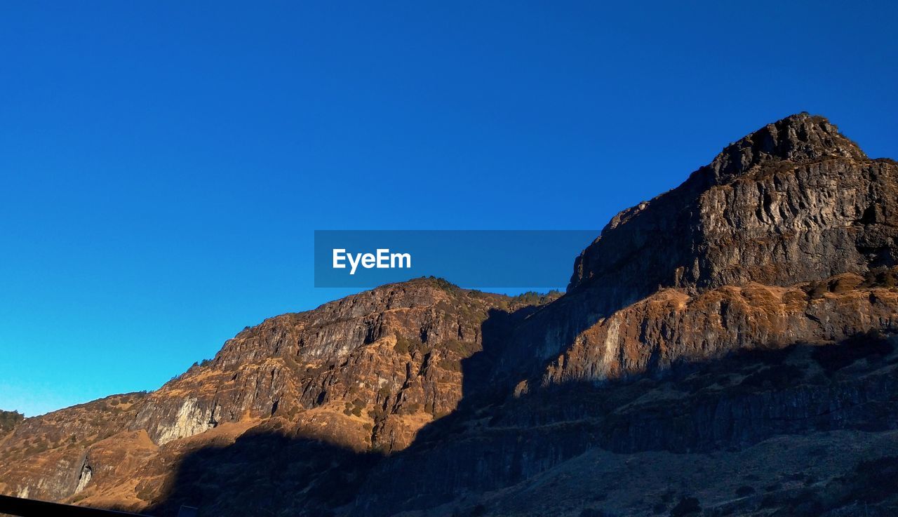 Low angle view of rock formation against clear blue sky