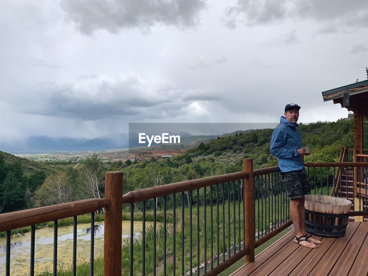 MAN STANDING ON RAILING AGAINST MOUNTAINS