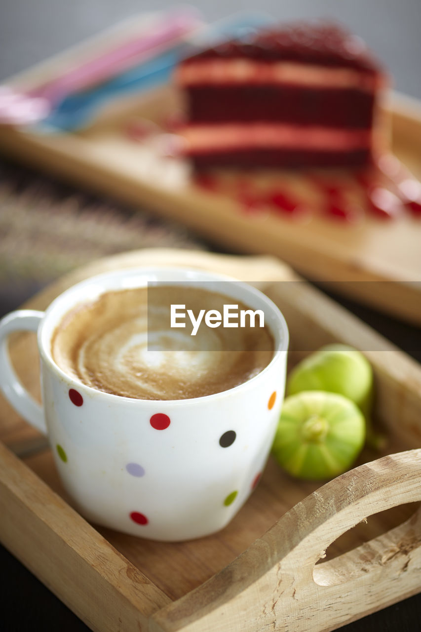 Close-up of coffee cup and figs in serving tray with red velvet cheesecake slice in background