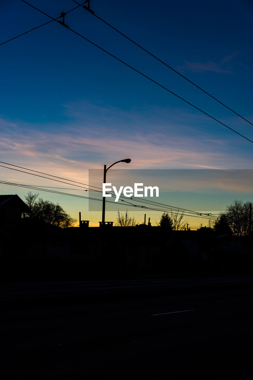 Low angle view of silhouette street light and cables against blue sky at dusk