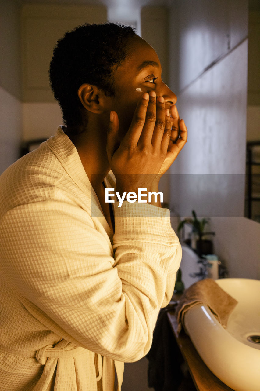 Young woman applying moisturizer on face at home