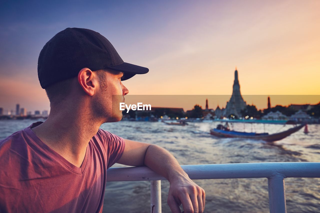 Close-up of man standing by railing at sea during sunset