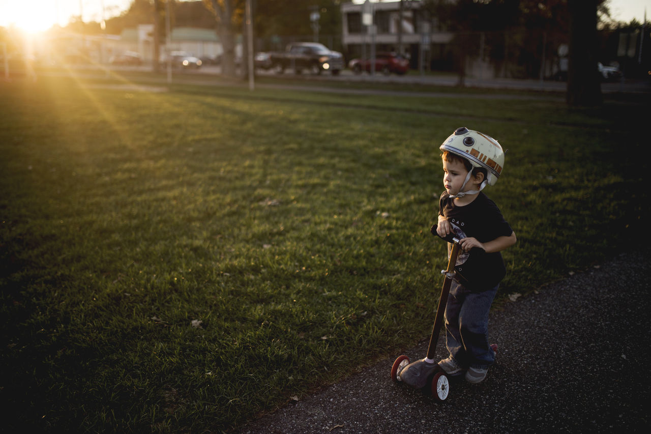 BOY STANDING ON GRASSY FIELD AGAINST TREES