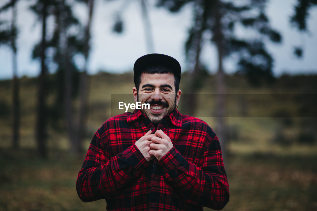 Cheerful man in casual wear standing among evergreen coniferous trees in autumn countryside