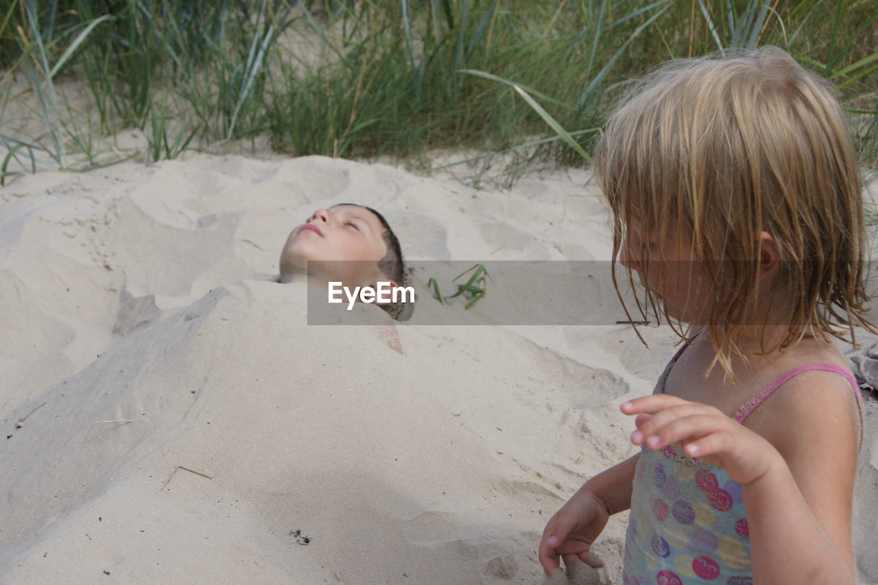 Cute girl buried brother in sand at beach